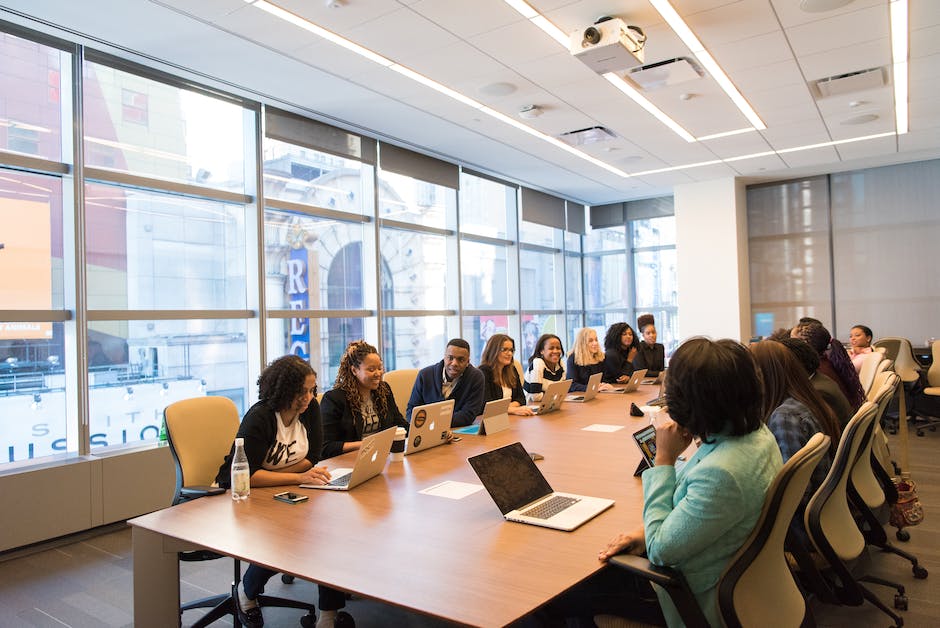 A diverse group of employees in a meeting room, discussing work-related topics.